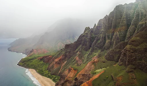 Steep, lush green volcanic cliffs of Madeira rising dramatically from the ocean into a misty mountain sky.